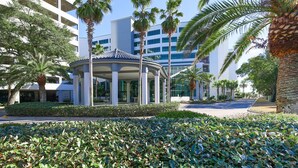 A modern building with a central pavilion surrounded by palm trees and a manicured garden.