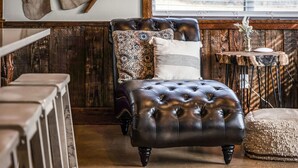 A leather sofa with patterned cushions, a wooden side table with a vase, and a rustic wooden wall. - Riverwalk | Pet-Friendly | Fishing | Deck | Grill (Kyle)