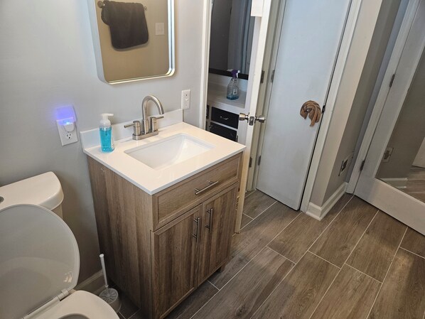 Un baño con lavamanos blanco, tocador de madera y espejo.