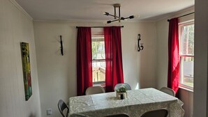 Zona pranzo con tavolo apparecchiato per quattro, tende rosse, lampadario e un quadro appeso al muro.