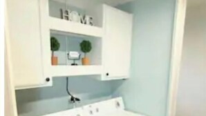 Una lavanderia funzionale con lavatrice, stendibiancheria e uno scaffale con piante in vaso.