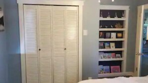 Una camera da letto con un letto, un armadio bianco e uno scaffale con libri e oggetti decorativi.
