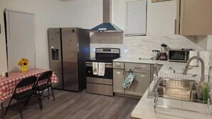 A compact kitchen with a refrigerator, stove, microwave, and sink. There is a dining table with chairs and a vase of flowers. - Entire Studio Apt + Patio + Lake View + Private (Charlotte)