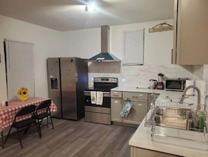 A compact kitchen with a refrigerator, stove, microwave, and sink. There is a dining table with chairs and a vase of flowers.