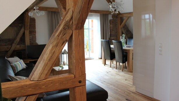A loft-style room with exposed wooden beams, a black leather sofa, a dining area with a table and chairs, and a large window providing natural light. - Exclusive, high-end ***** vacation rental with a large garden (Freiamt)