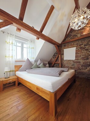 Een slaapkamer met een schuine kap, houten balken, een bed met kussens, een nachtkastje, een lamp en een stenen muur.
