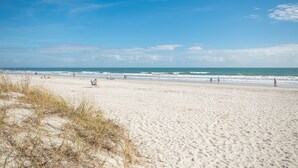 Una playa arenosa con gente caminando y sentada, y el océano al fondo.