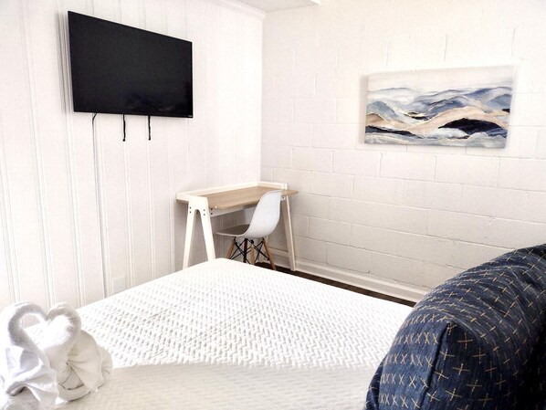 Ett sovrum med en säng, ett skrivbord, en stol, en tv och en tavla på väggen.