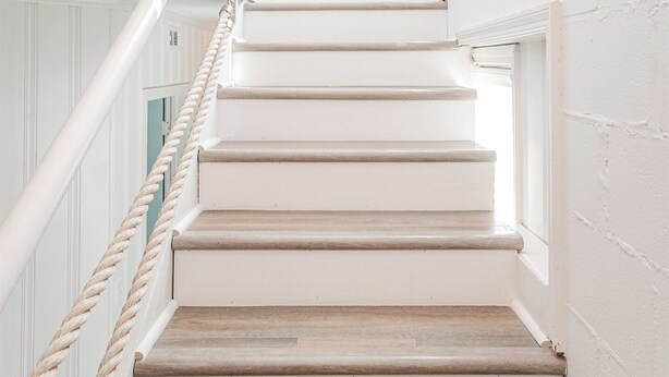 Una escalera con barandillas blancas y escalones de madera que llevan a una plataforma con vista al cielo.