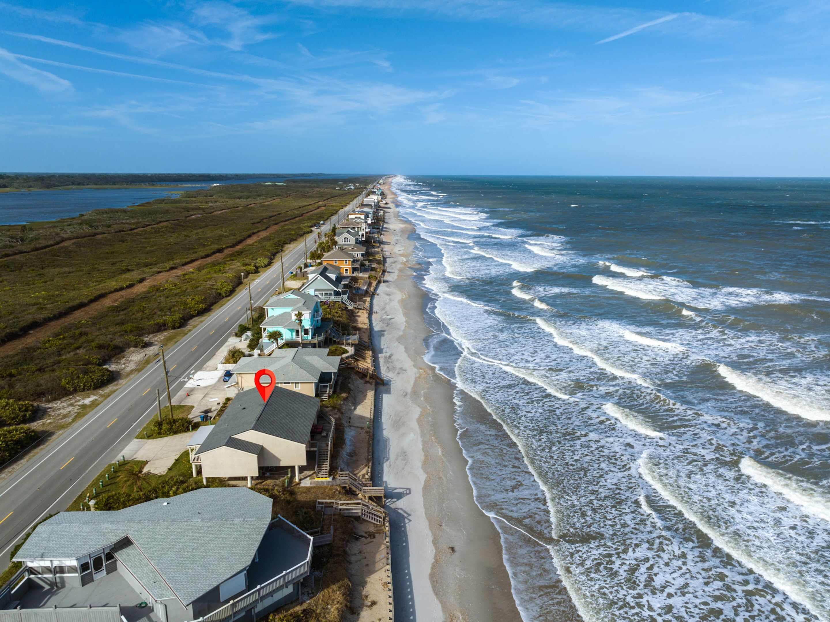 A coastal road lined with houses, a beach, and a road with a red location marker.