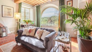 Ein gemütliches Wohnzimmer mit einer Ledersofa, einem kleinen Tisch mit Gläsern und Flaschen, einem Blumentopf und Blick durch ein Fenster.