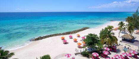 A beach resort with a pool, sun loungers, and umbrellas.
