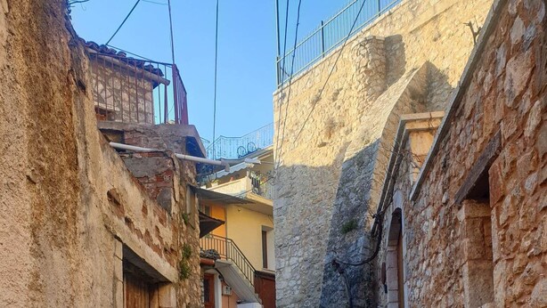 Una estrecha calle empedrada bordeada por edificios antiguos de piedra con puertas y balcones de madera.