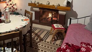 Una habitación acogedora con chimenea, una mesa de comedor con mantel floreado y un taburete pequeño.