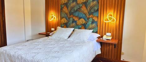 A neatly made bed with a patterned bedspread, wooden headboard with leaf-patterned wallpaper, and bedside lamps with glowing light fixtures.