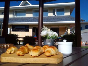 A table with croissants, a white pot, and a bouquet of flowers. - CASA HIDALGO ECUADOR (Cumbayá)
