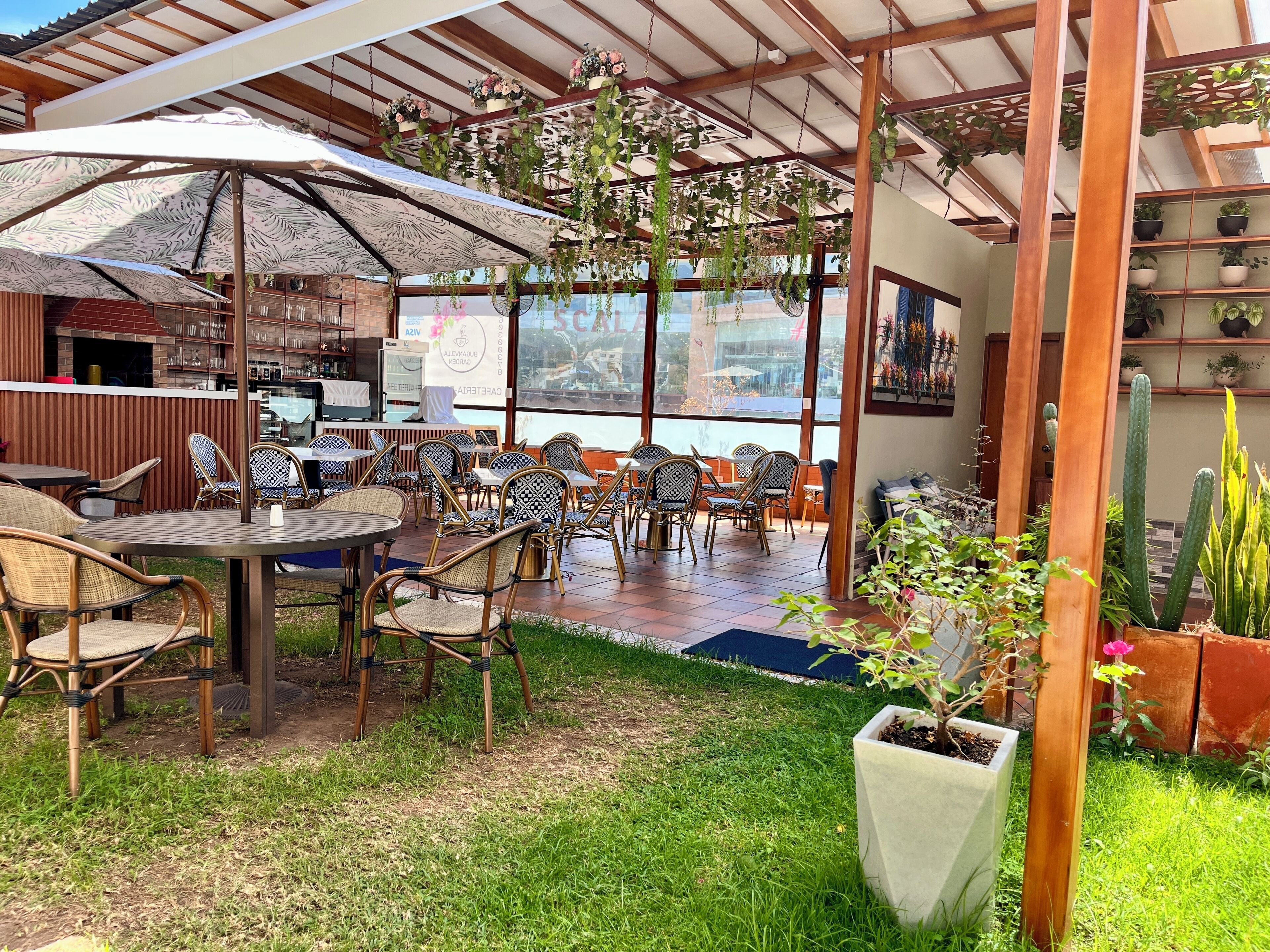 An outdoor patio with tables and chairs, a covered area with hanging plants, and a view of the cityscape through large windows.