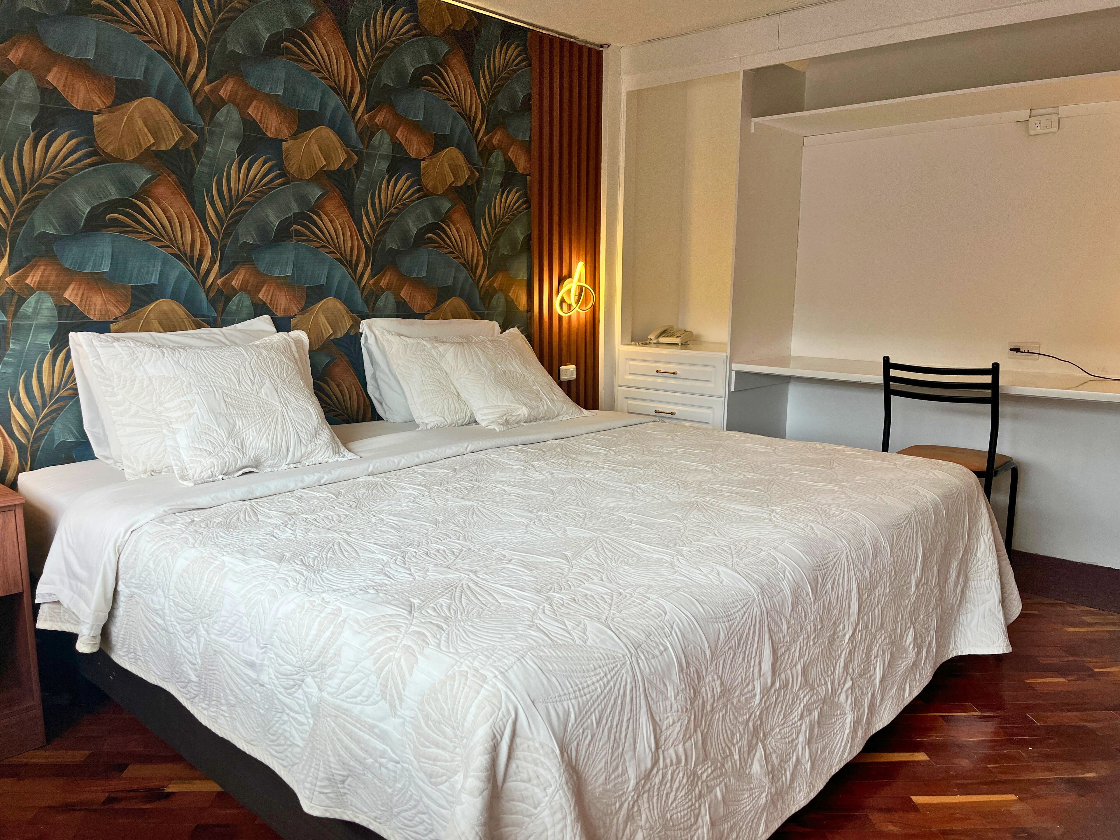 Ein Schlafzimmer mit einem großen Bett, einem Nachttisch, einer Kommode, einem Sessel und einer Wand mit einem Blattmuster.