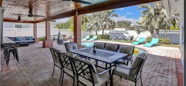 Un patio exterior con una mesa y sillas, una silla colgante y un área de piscina con sillas de descanso.