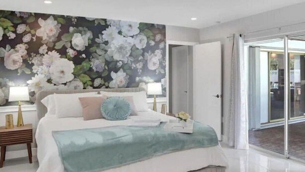 A bedroom with a large bed, floral wallpaper, and a view through a glass door.