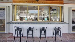 A bar area with a wooden ceiling, a ceiling fan, and three black bar stools.