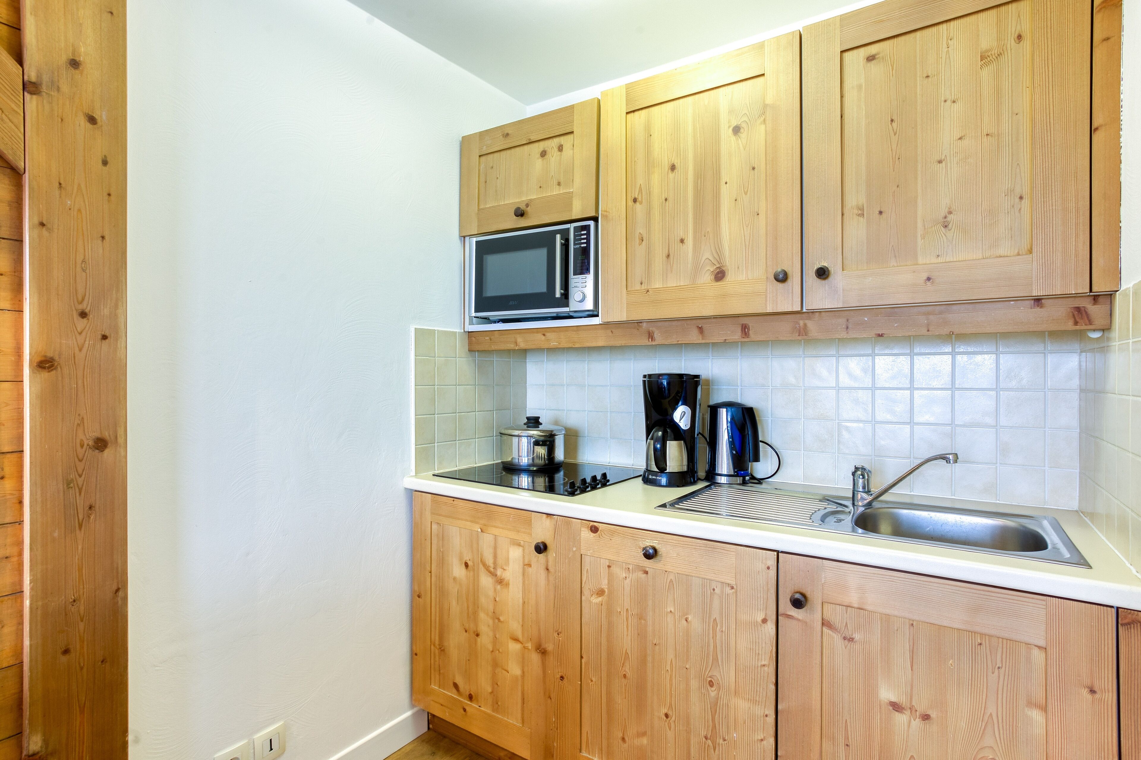 A compact kitchen with wooden cabinets, a microwave, a coffee maker, and a sink.