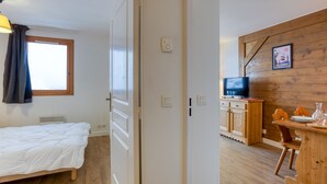 A bedroom with a bed, a wooden desk, a television, and a dining area.
