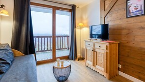 A room with a bed, a television on a wooden cabinet, a small round table, and a balcony with a view.