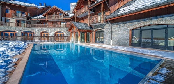 A pool area with a clear blue pool, stone walls, and wooden buildings with balconies.