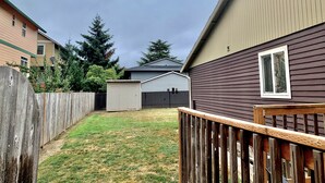 Un jardin à l’arrière d’une maison, avec une terrasse en bois, un abri de jardin et une maison dont les murs sont recouverts de bardage.