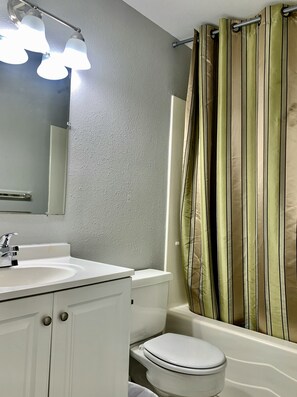 Une salle de bain avec un lavabo blanc, un miroir et des toilettes. Il y a un rideau de douche à rayures verticales.