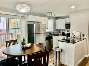 A modern kitchen with white cabinets, a stainless steel refrigerator, a dining table with chairs, and a hanging light fixture. - 2 BR Single Story Townhouse w King Bed (Beaverton)