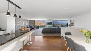 A modern kitchen with a bar area, a dining table with chairs, and a view of a mountainous landscape. - Remarkable Lake View Modern Executive Home (Queenstown)