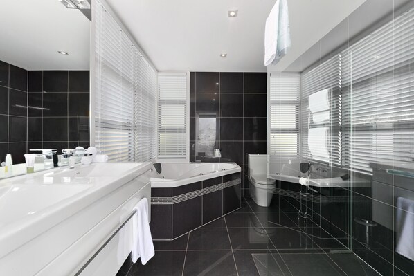 A modern bathroom with a large bathtub, a separate shower area, and a vanity with a mirror. - Remarkable Lake View Modern Executive Home (Queenstown)