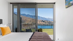 A bedroom with a large bed, a sliding glass door leading to a balcony with a mountain view. - Remarkable Lake View Modern Executive Home (Queenstown)