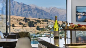A dining area with a mountain view, a bottle of wine, and a fruit platter. - Remarkable Lake View Modern Executive Home (Queenstown)