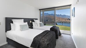 A bedroom with two beds, a large window with a mountain view, and a sliding glass door. - Remarkable Lake View Modern Executive Home (Queenstown)