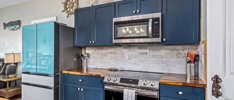 A kitchen with blue cabinets, a microwave, a stove, and a sink.