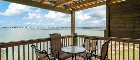 A covered outdoor seating area with a table and chairs, overlooking a body of water and distant shoreline.