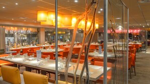 Ein Restaurant mit mehreren Tischen und orangefarbenen Stühlen, das modernes Ambiente mit Glastrennsteinen und warmer Beleuchtung bietet.