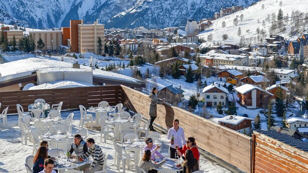 Ein mit Schnee bedeckter Außenbereich zum Essen mit Tischen und Stühlen, mit Blick auf eine Berglandschaft.