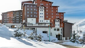 Ein mehrstöckiges Hotel mit Blick auf ein Skigebiet, mit einer markanten Eingangspforte und verschneiter Landschaft.