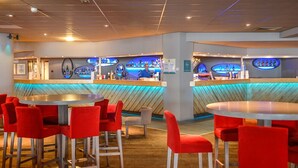 Eine Bar mit roten Stühlen und Tischen, einer Theke mit Bartender und einer Holzbalkendecke.