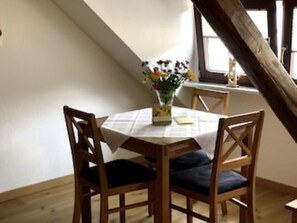 A dining area with a table set for two, wooden chairs, a vase with flowers, and a window with a view. - Herbstlaub Vacation Rental, stunning view of the countryside (Minheim)