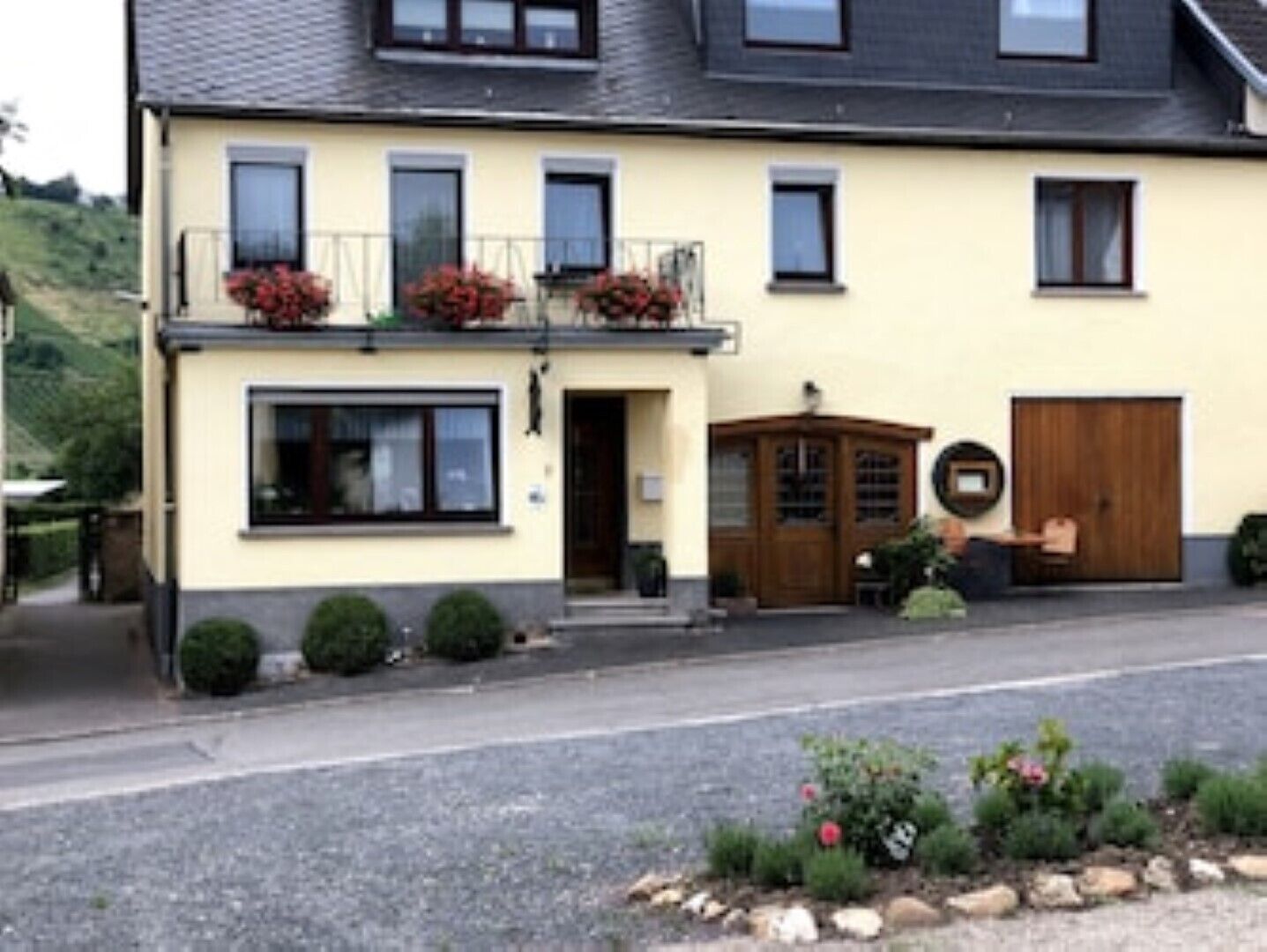 Ein zweistöckiges Gebäude mit Balkon, Eingangstür und einem kleinen Garten mit Pflanzen und Blumen.