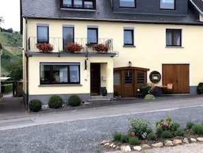 En toetagers bygning med balkon, hoveddør og en lille have med planter og blomster.