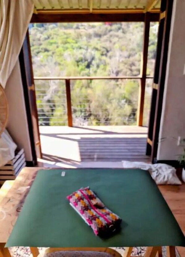 A room with a green bed, a window with a view of trees, and a wooden table.