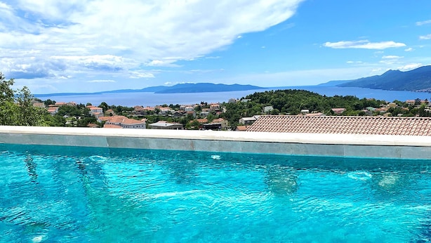 Una piscina azul cristalina con vistas a una zona residencial y montañas al fondo.