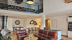 A spacious living area with leather sofas, a wooden coffee table, and a dining table. A staircase with a railing leads to an upper level. - Farmhouse with a private heated indoor pool. Near Alsace. (Entre-Deux-Eaux)