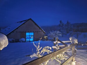 Paisatge cobert de neu amb una cabana de fusta i una tanca de fusta.